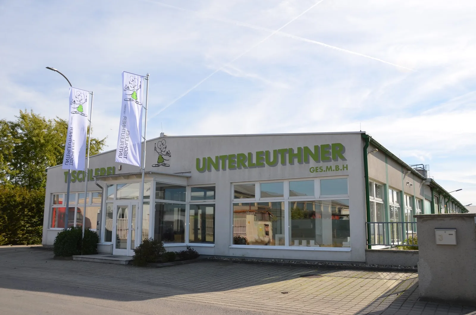 Firmengebäude der Tischlerei Unterleuthner mit grünem Schriftzug, Maskottchen und zwei Fahnen