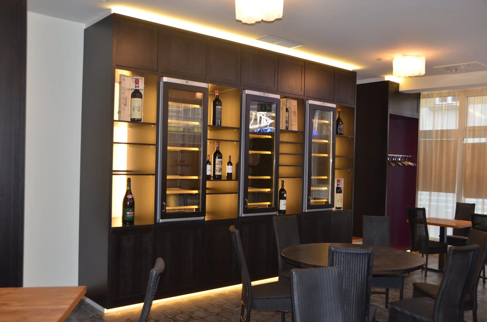 Weinwand mit gläsernen Weinschränken und dunklem Holz, davor Tische und Stühle