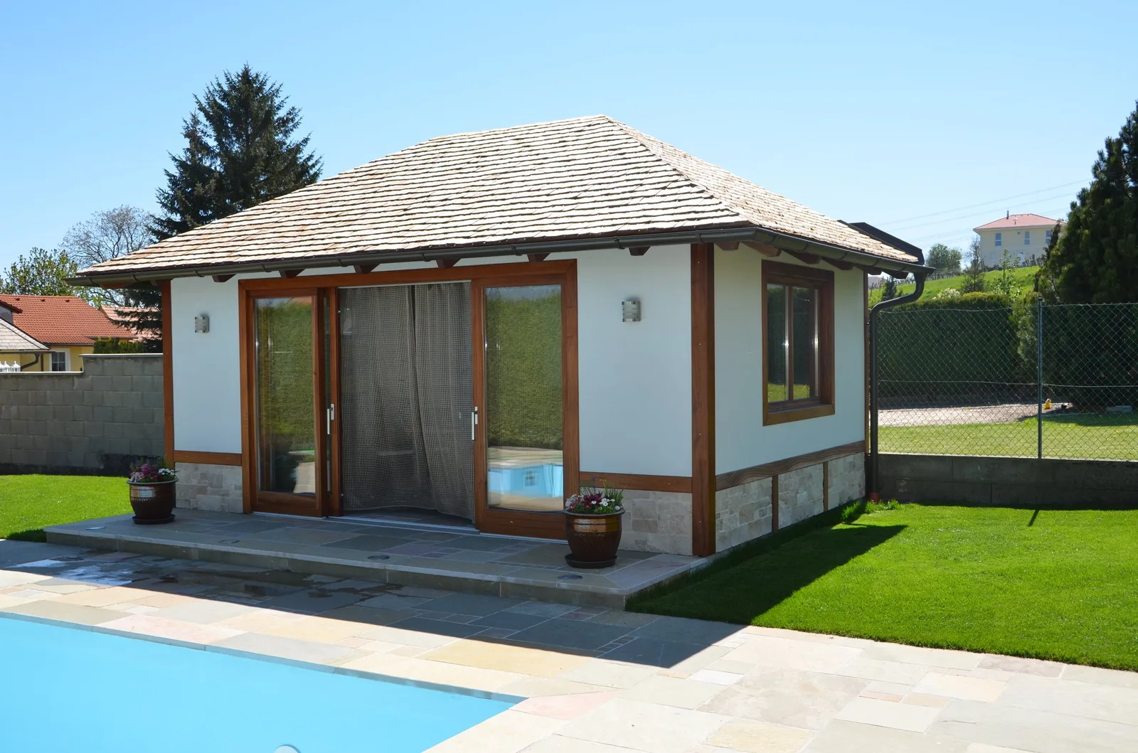 Gartenhaus mit großen Holzfenstern neben einem Pool