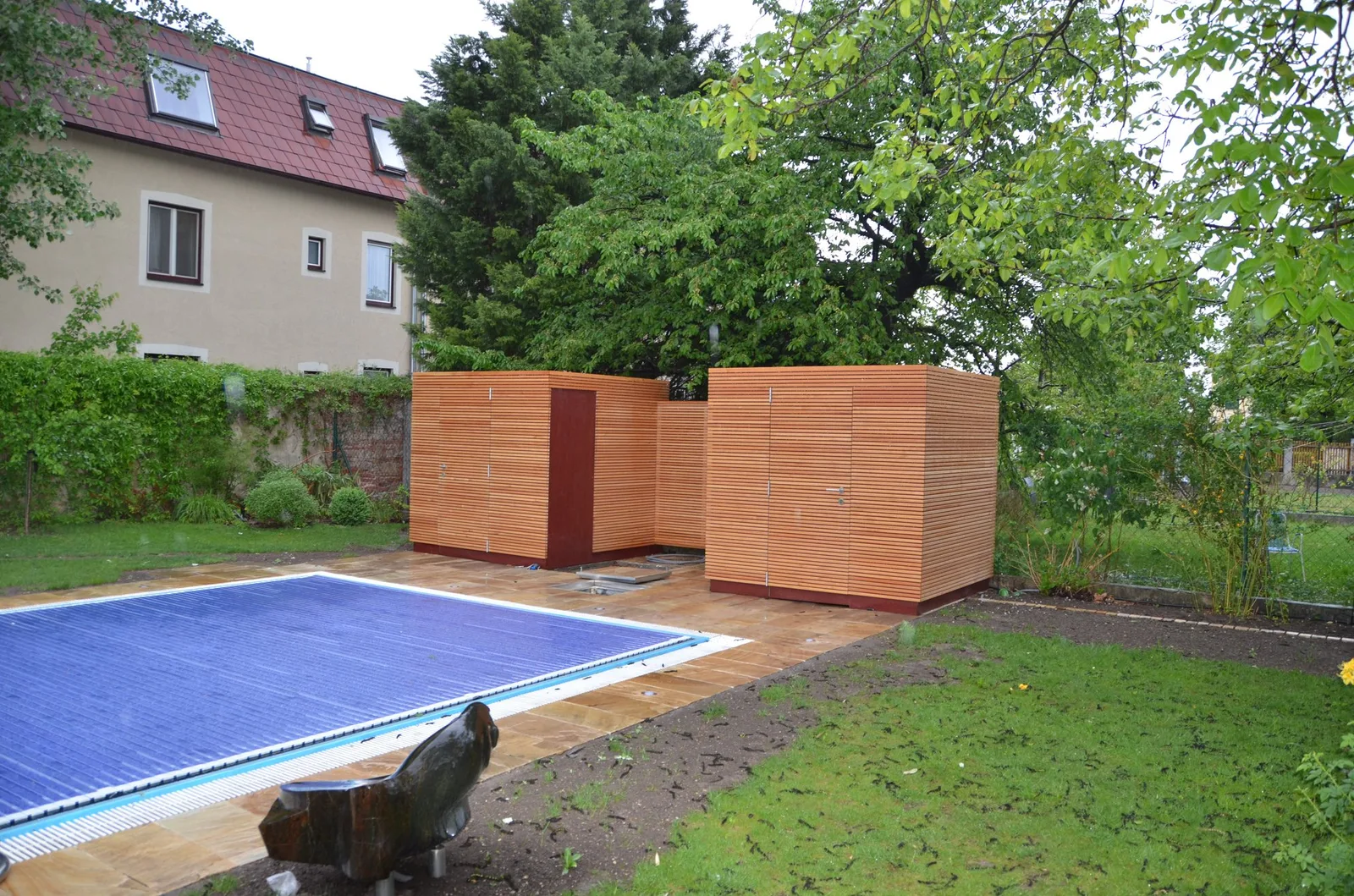 Häuschen aus waagrechten Holzlatten neben einem Pool im Garten