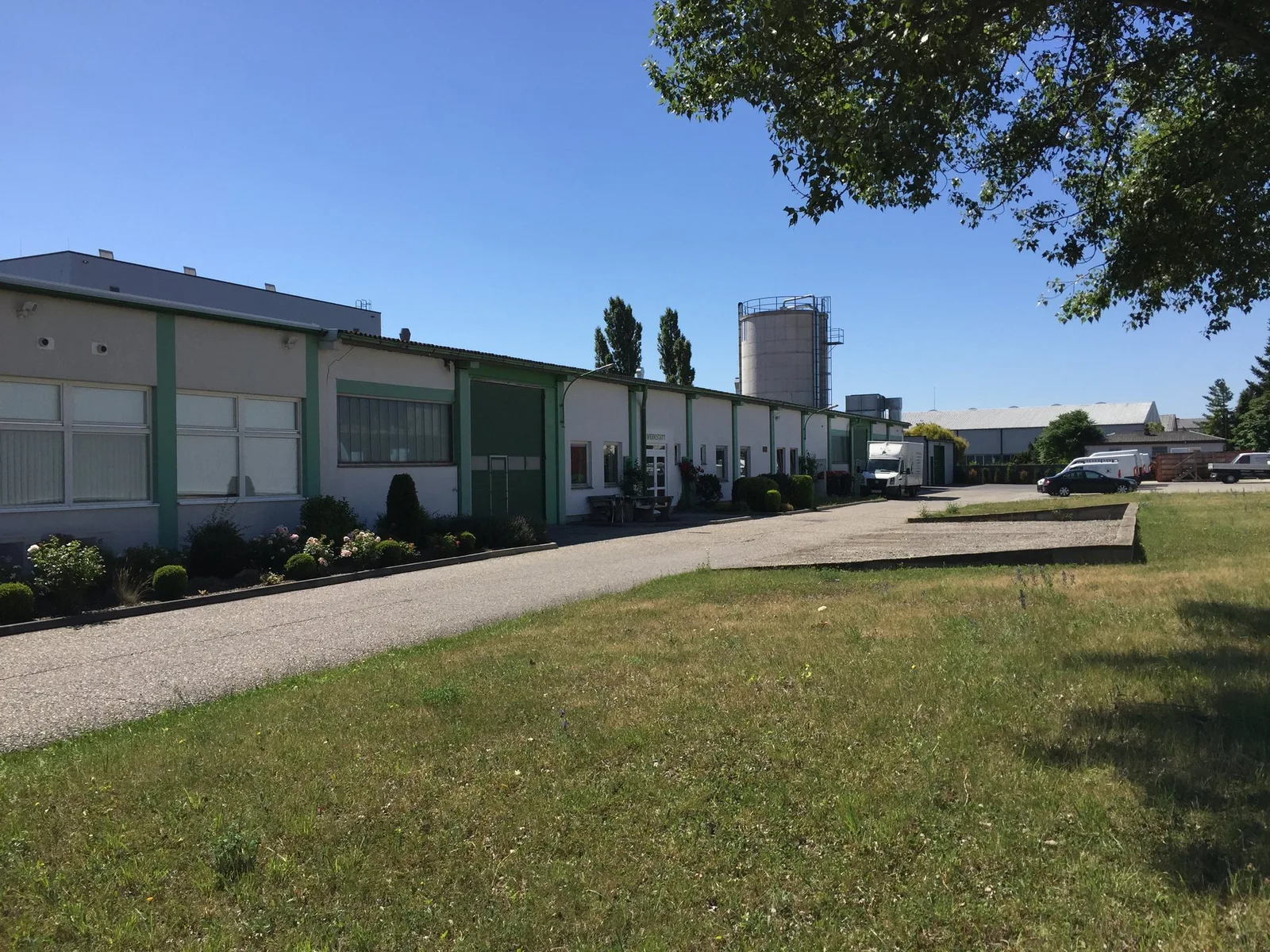 Werkhallen der Tischlerei mit Silo, davor eine Wiese